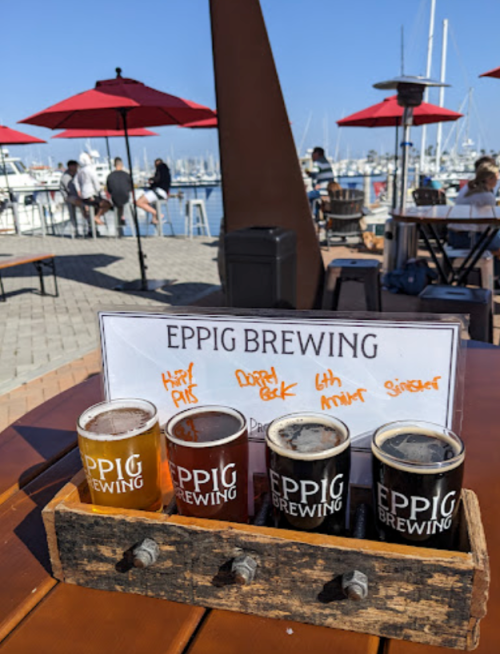 A wooden flight of four craft beers sits on a table with a marina view, featuring Eppig Brewing branding.