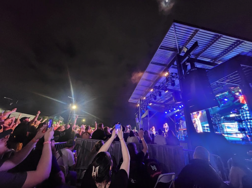 A lively concert scene at night, with a crowd raising their hands in front of a brightly lit stage.