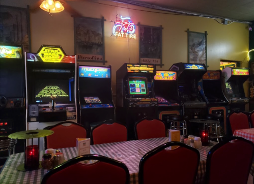 A cozy arcade with vintage game machines and a neon sign, set in a restaurant with checkered tablecloths.