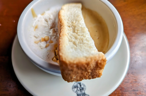 A bowl of soup with a slice of toasted bread resting on the edge, served on a small plate.