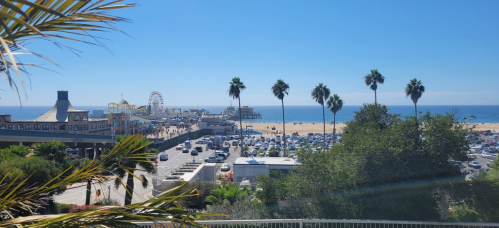 A sunny view of Santa Monica beach with palm trees, a pier, and a ferris wheel in the background.