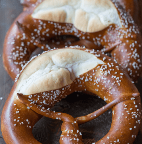 Close-up of freshly baked pretzels sprinkled with coarse salt on a wooden surface.