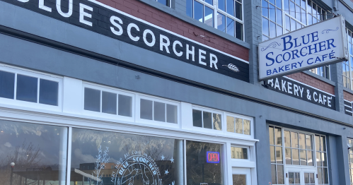 Exterior of Blue Scorcher Bakery & Café, featuring colorful chairs outside and large windows with a welcoming sign.