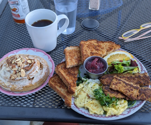 A plate of scrambled eggs, toast, and a side salad, with a cinnamon roll and coffee on the side.