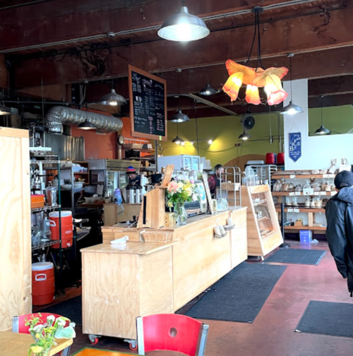A cozy café interior with wooden counters, a menu board, and colorful decor, featuring flowers and warm lighting.