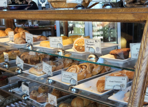 A display case filled with various baked goods, including pastries, cakes, and muffins, each labeled with prices.