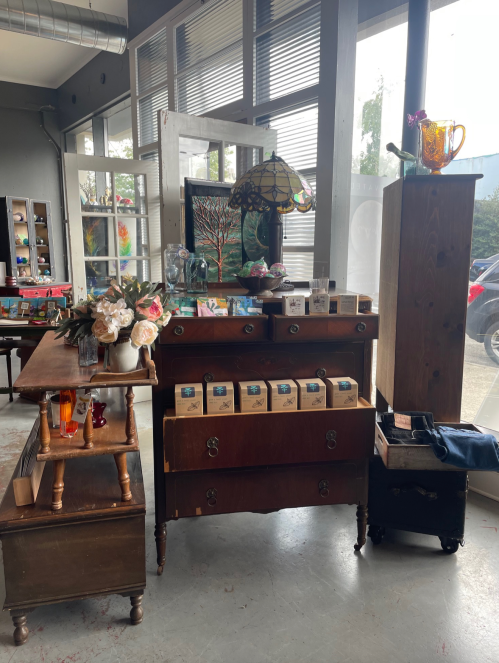 A cozy vintage shop interior featuring a wooden dresser, a table with decor, and various items displayed on shelves.