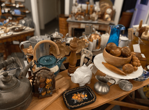 A collection of vintage items, including teapots, wooden bowls, and decorative objects, displayed on a wooden table.