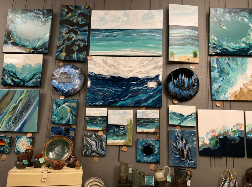 A gallery wall featuring various abstract paintings in shades of blue, green, and white, with textured designs.