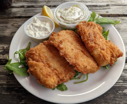 Three golden-brown fried fish fillets on a bed of greens, served with lemon and dipping sauces.