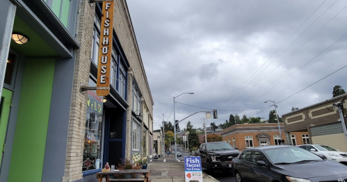 A street view of a fish house restaurant with a sign for fish tacos, cloudy skies, and parked cars nearby.