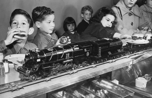 Children enjoying a meal at a diner, with a toy train delivering food along the counter.