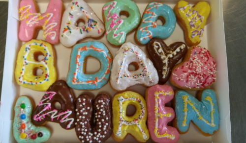 A box of colorful donuts arranged to spell "HAPPY BIRTHDAY LAUREN" with various icing and sprinkles.