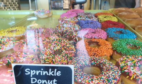 A display of colorful donuts with various sprinkles, including pink, orange, purple, and rainbow toppings.