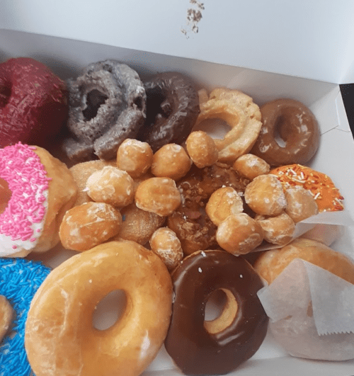 A box filled with various donuts, including glazed, chocolate, and sprinkled varieties, along with donut holes.
