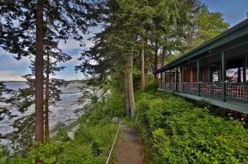 A scenic view of a pathway leading to a house surrounded by trees, overlooking a beach and water in the distance.