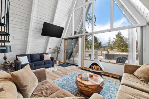 Cozy A-frame living room with large windows, modern decor, a fireplace, and a view of the outdoors.