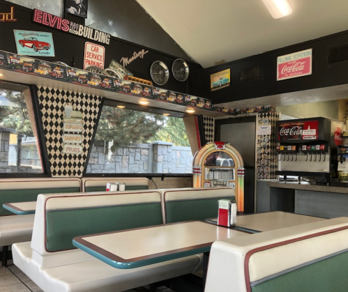 Retro diner interior with green booths, a jukebox, and vintage decor featuring cars and Coca-Cola memorabilia.
