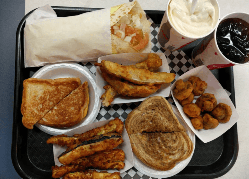 A tray of various fast food items including a taco, fried fish, toast, and drinks.