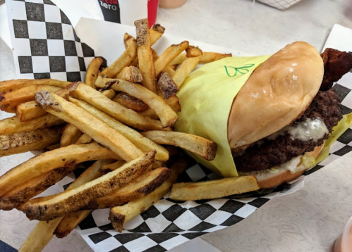 A burger wrapped in yellow paper with fries on the side, served in a checkered basket.
