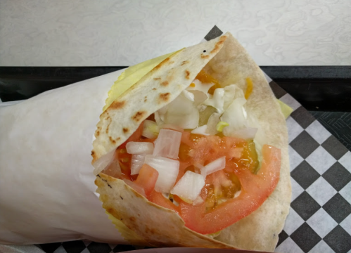 A close-up of a taco wrapped in paper, filled with lettuce, tomato, onions, and sauce in a soft tortilla.