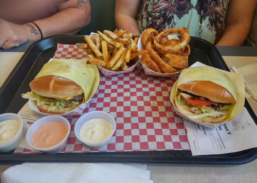 A tray with two wrapped burgers, fries, onion rings, and dipping sauces on a checkered paper background.
