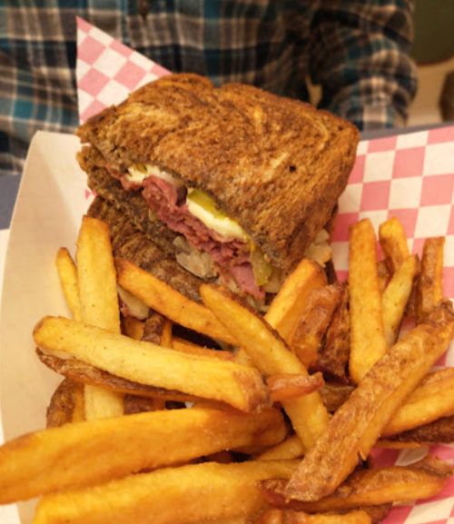 A hearty sandwich with layers of meat and toppings, served with a side of golden French fries on a checkered paper.