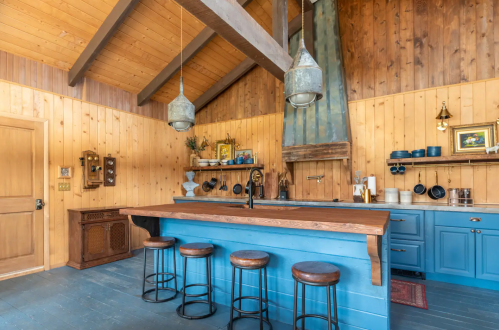 Cozy kitchen with wooden walls, blue cabinetry, a large island, and rustic bar stools under pendant lights.