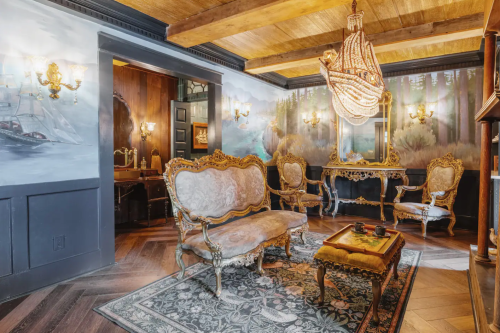 Elegant vintage sitting area with ornate furniture, a chandelier, and scenic wall murals in a cozy, well-lit room.