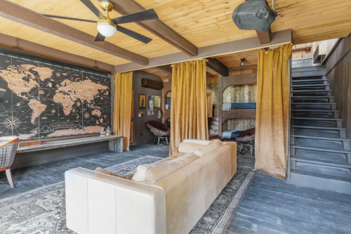 Cozy interior with a map wall, a sofa, curtains, and a staircase leading to an upper level. Warm, inviting atmosphere.