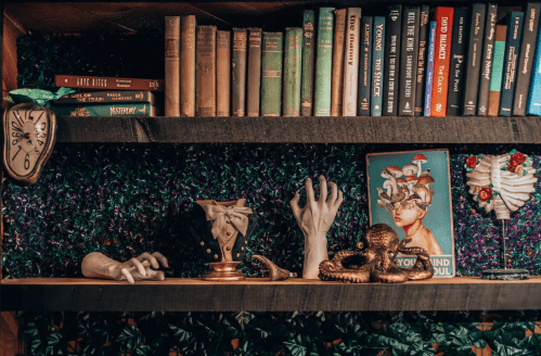 A shelf with vintage books, decorative hands, an octopus, and a surreal art piece against a green backdrop.