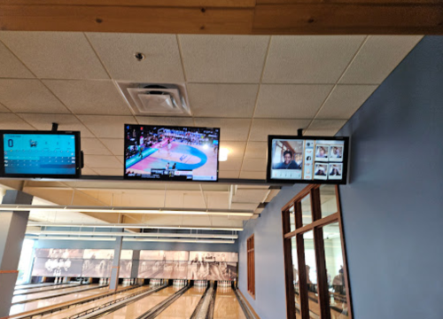 Two screens display a basketball game and bowling scores in a bowling alley. The interior is bright and spacious.