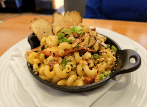 A skillet of macaroni and cheese topped with green onions and crispy bread, served on a white plate.