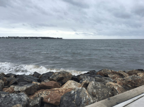 A rocky shoreline with waves lapping against the stones under a cloudy sky.