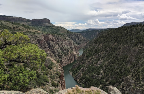 A scenic view of a winding river surrounded by steep, rocky cliffs and lush greenery under a cloudy sky.