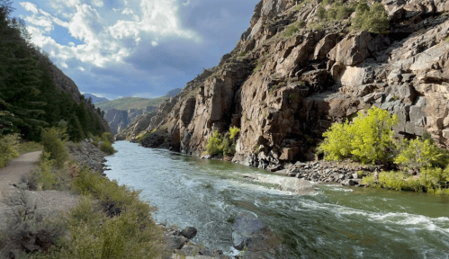 A serene river flows between rocky cliffs, surrounded by lush greenery under a partly cloudy sky.