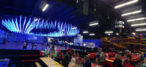 A vibrant indoor play area with colorful lighting, kids skating, and families seated at tables.