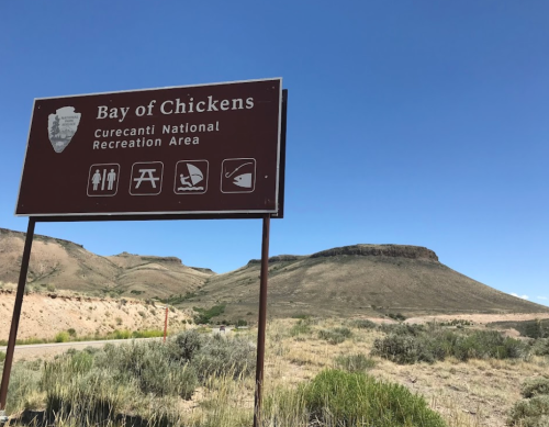 Sign for Bay of Chickens at Currecanti National Recreation Area, with a mountainous landscape and clear blue sky in the background.