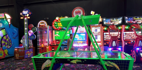 A vibrant arcade scene featuring colorful games, neon lights, and a green air hockey table in the foreground.
