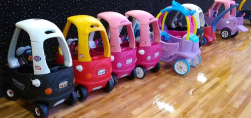 A row of colorful toy cars and carriages lined up on a wooden floor in a play area.