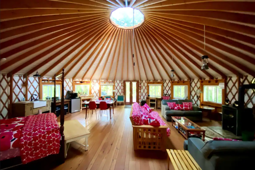 Interior of a spacious yurt with wooden beams, cozy seating, and large windows, creating a warm, inviting atmosphere.