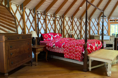 Cozy yurt interior featuring a bed with a red floral blanket, wooden furniture, and a warm, rustic atmosphere.