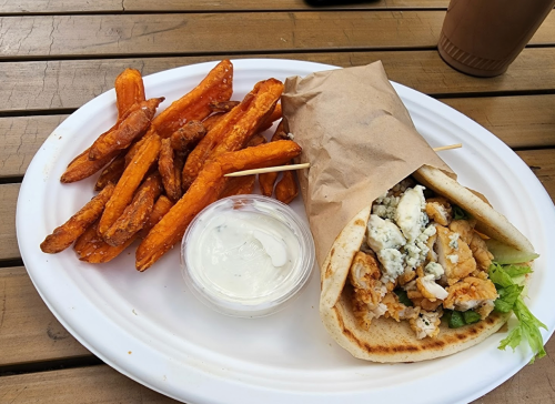 A plate with a wrapped sandwich filled with chicken and lettuce, accompanied by sweet potato fries and a dipping sauce.