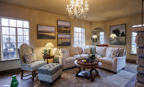 Cozy living room with a chandelier, soft seating, artwork on the walls, and large windows letting in natural light.