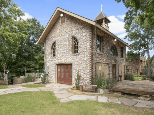 A charming stone house with a peaked roof, surrounded by greenery and a stone pathway.