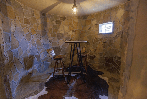 Cozy stone room with a small table, two wooden chairs, and a window, illuminated by a hanging lantern.