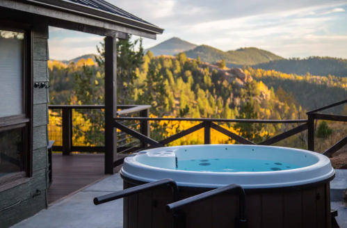A hot tub on a deck with a scenic view of mountains and trees under a cloudy sky.