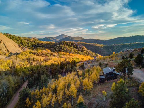A scenic view of mountains and trees with autumn foliage, featuring a small house nestled in the landscape.
