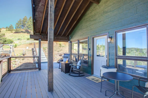A cozy porch with rocking chairs and a small table, surrounded by nature and a clear blue sky.