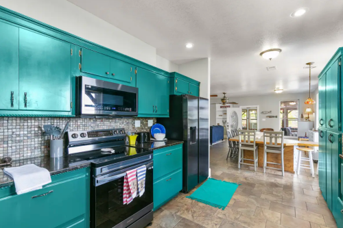 Bright kitchen with teal cabinets, stainless steel appliances, and a dining area visible in the background.